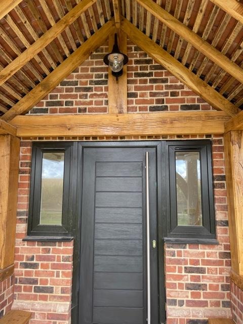The Nook — oak porch with exposed rafters, brick gable and black composite front door